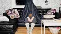 A woman sits on a sofa with a blanket over her head. 
