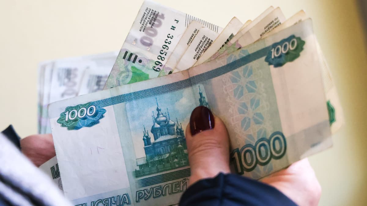 Nippu automaatista nostettuja ruplan seteleitä naisen kädessä. Päällimmäisenä tuhannen ruplan seteli.