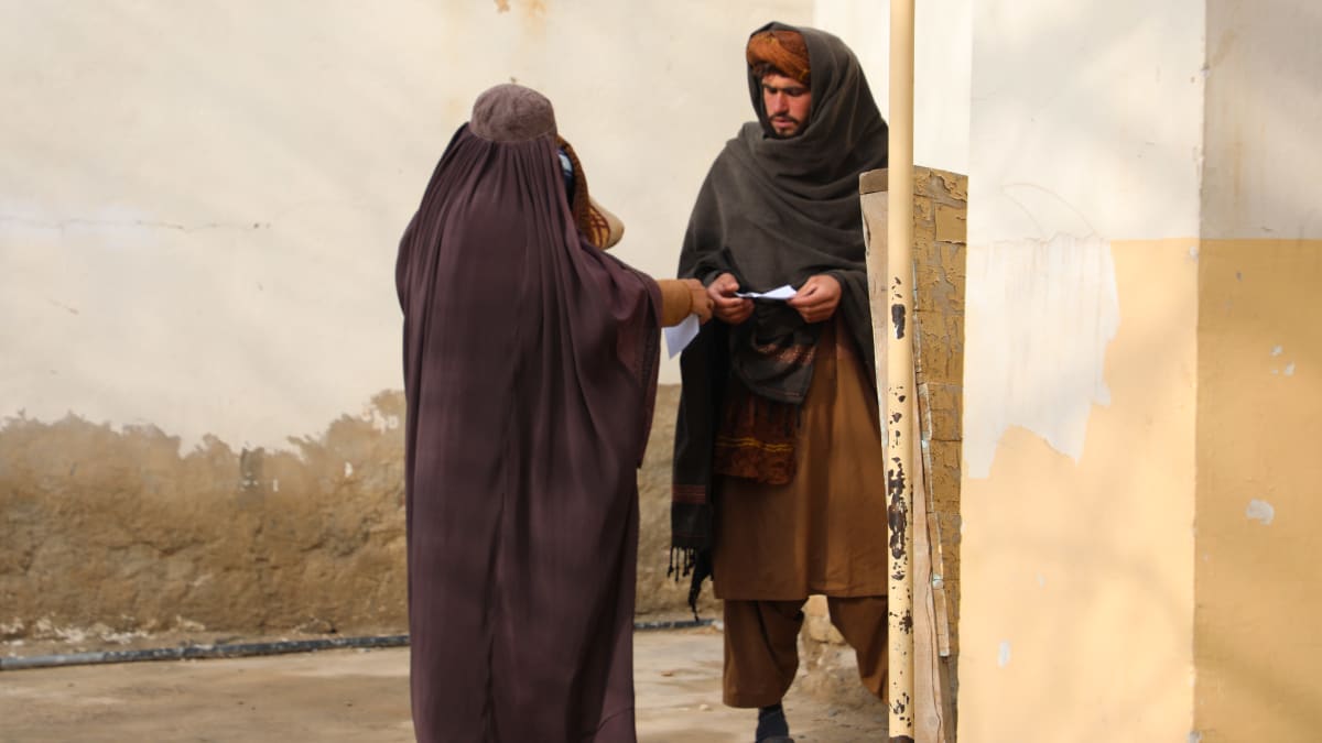 Nainen ojentaa lääkereseptiä miehelleen klinikan pihalla Afganistanissa.