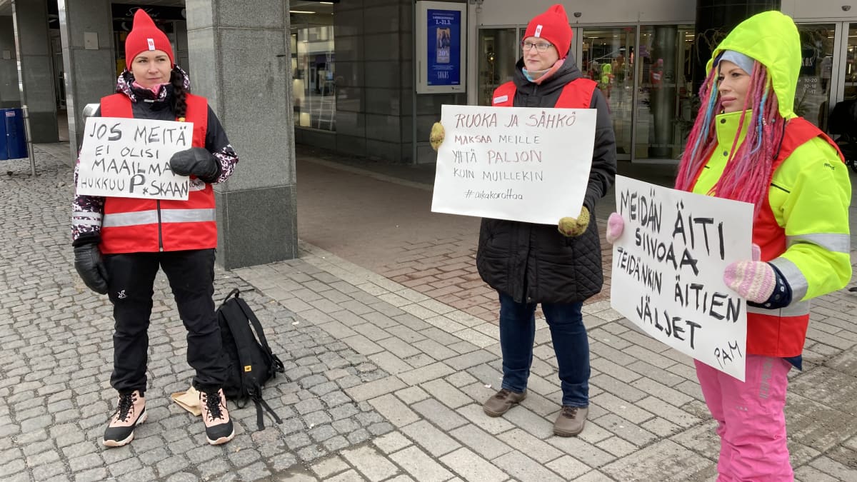 Kuvassa kolme naista, jotka ovat kiinteistöpalvelualan lakossa seisomassa Jyväskylän keskustassa banderollien kanssa.