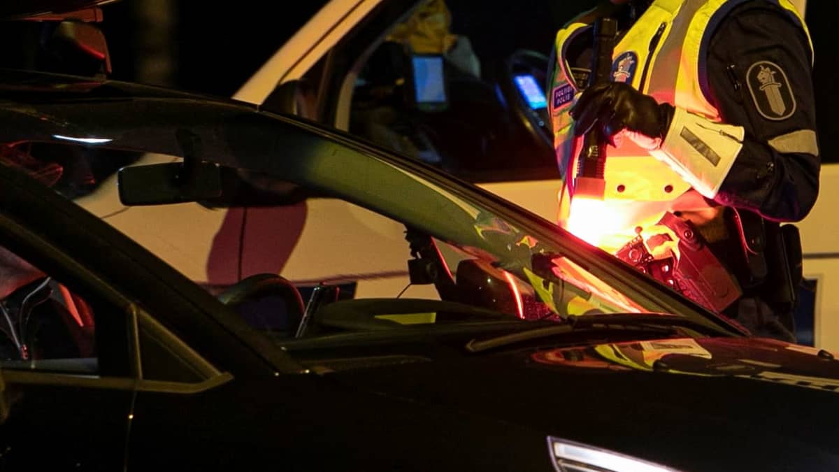 Poliisi tarkastamassa autoa taskulampun valossa.