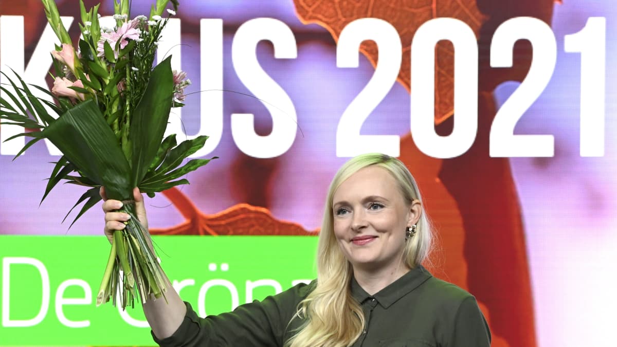 Maria Ohisalo håller upp en bukett med blommor och ler medan hon tittar åt sidan. 
