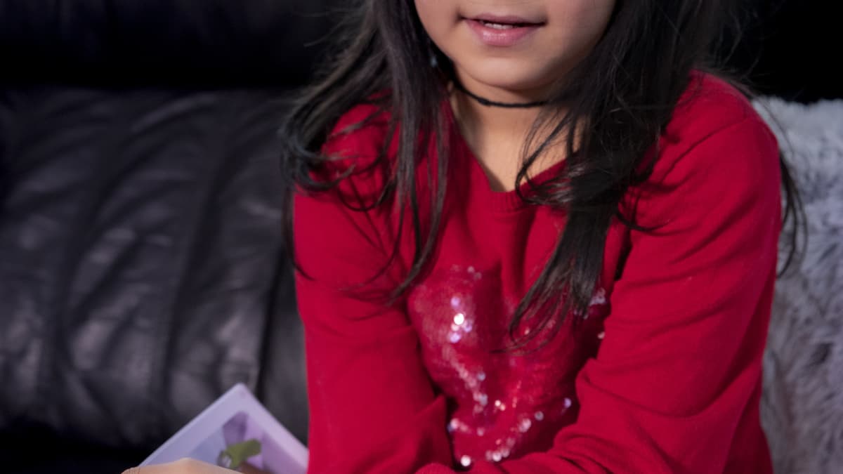 Husna Azimi istuu kotona sohvalla koulukirja kädessä.