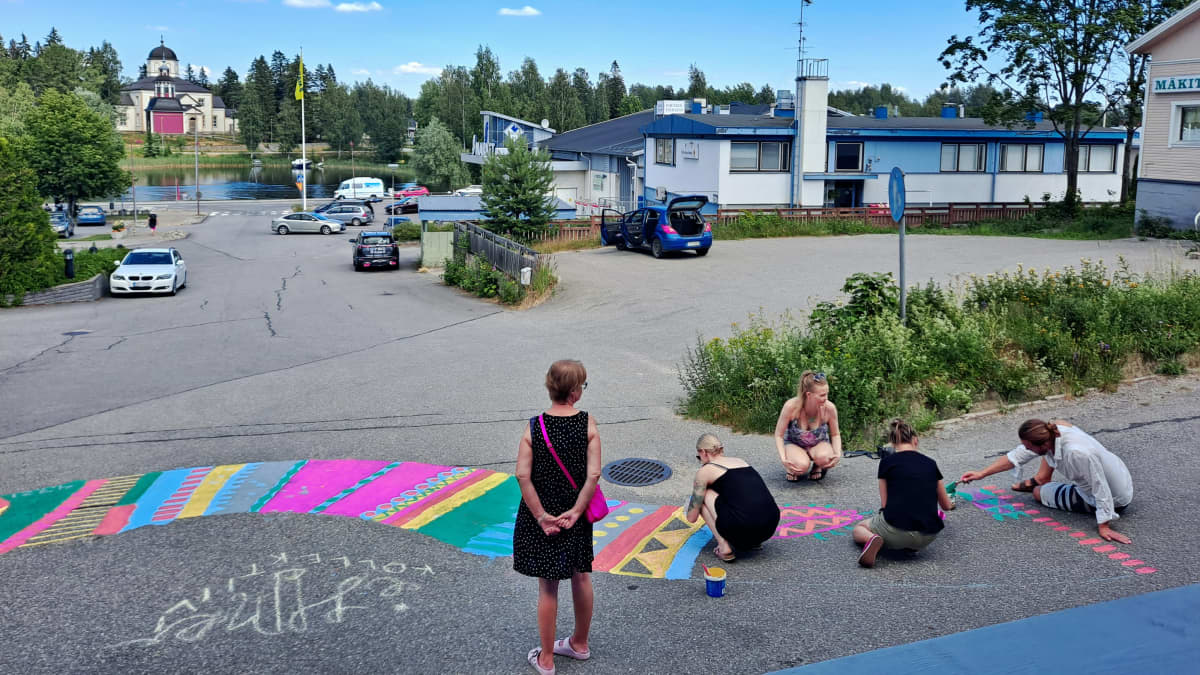 Sulkavalaisen Ihmekollektiivin jäsenet maalaavat kirjavaa räsymattoa asfalttiin. 