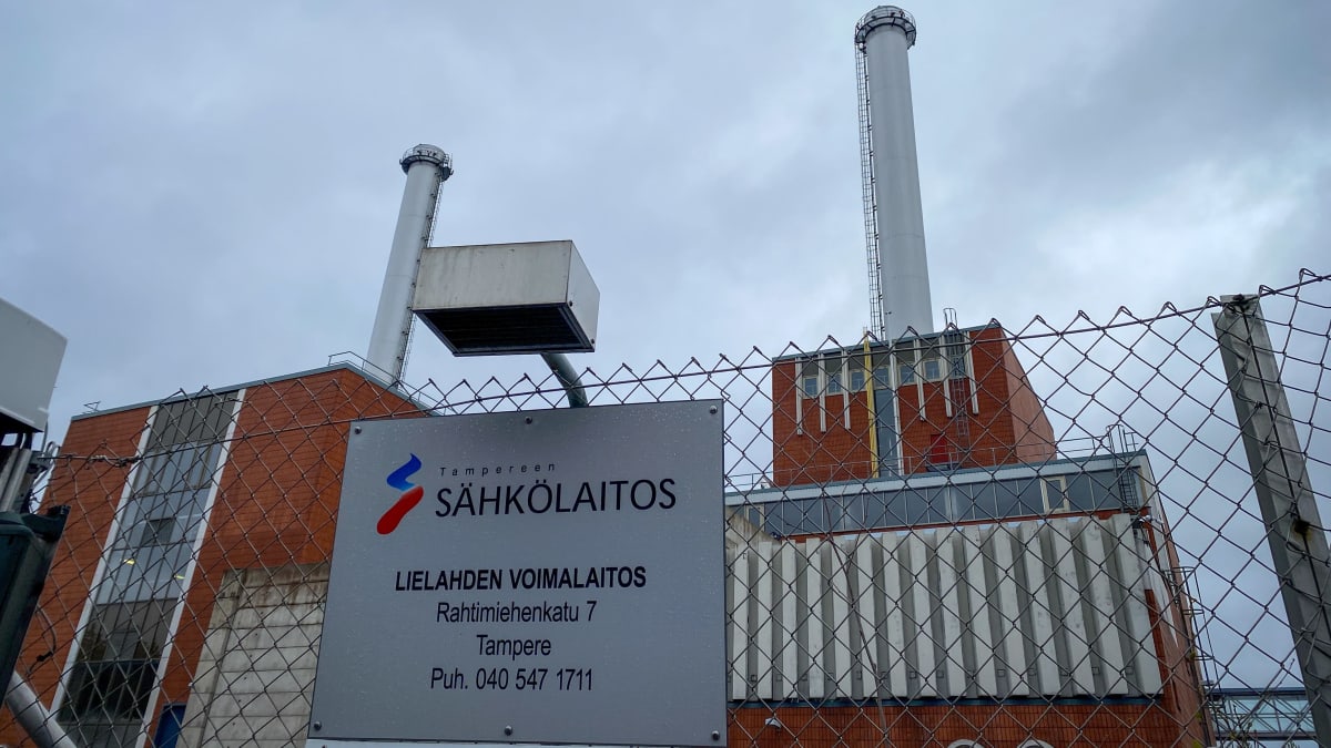Tampereen Sähkölaitoksen Lielahden voimalaitos kuvattuna ulkoapäin. Tiilistä rakennettu, massiivinen laitos, josta nousee useampi korkea piippu. Taustalla pilvinen taivas.