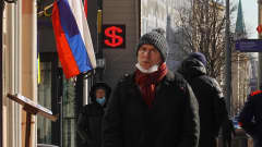 Moskovalaisia kävelee kadulla, taustalla Venäjän lippu ja dollarin merkki.