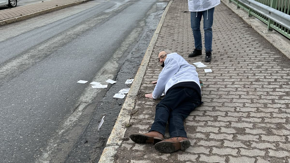 Ben Zyskowicz makaa kadulla, avustaja ottaa kuvaa kännykällä.