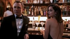 Bond i smoking stående vid en bardisk med kvinna i vacker klänning.