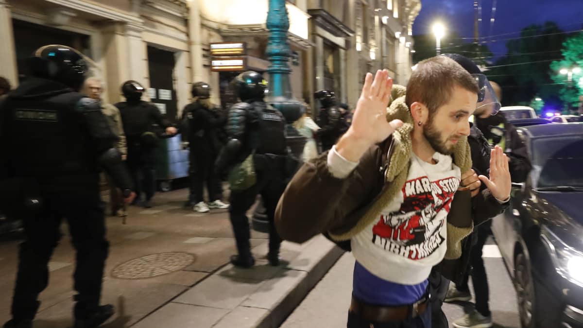Nuori mies kiinniotettuna mielenosoituksissa Pietarissa. Hän pitää käsiään ylhäällä. Taustalla näkyy paljon poliiseja.