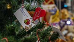 Joulukuusessa olevia kortteja, joissa tietoja lahjan saajista ja Hyvää joulua -koriste.