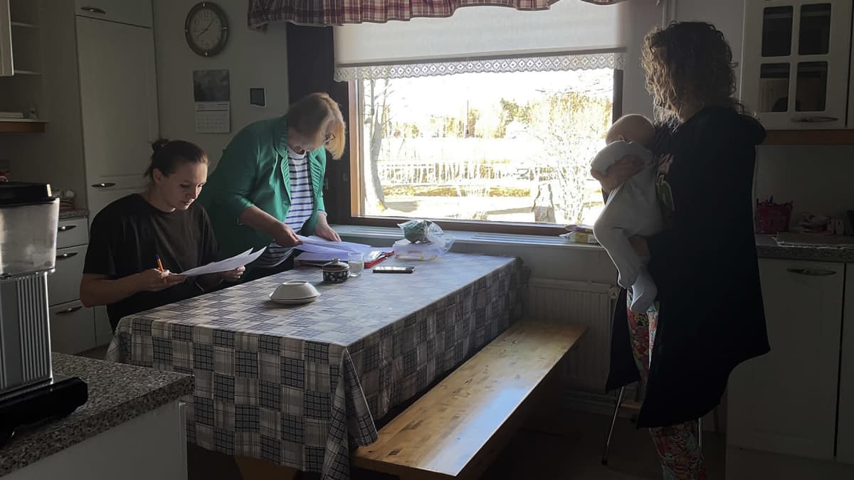 Vapaaehtoinen Elina Viljamaa pitelee ukrainalaisperheen vauvaa sillä välin, kun äiti ja isoäiti täyttävät lomakkeita.