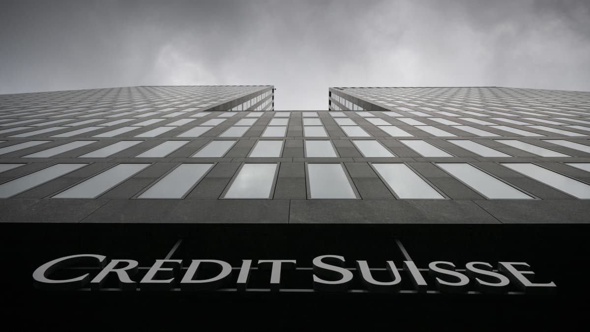 Näkymä harmaasta korkeasta liikerakennuksesta suoraan rakennuksen juurelta ylöspäin katsottuna, taivaalla harmaita pilviä ja alareunassa Credit Suissen logo.