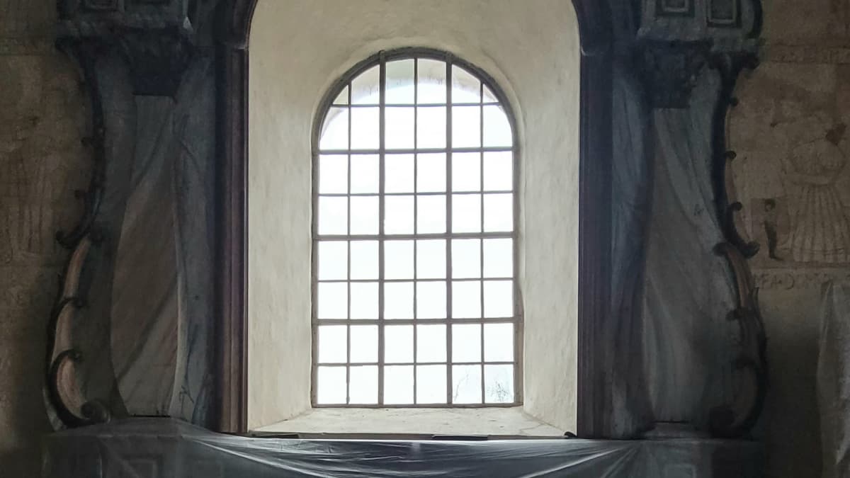 Ikkuna Isonkyrön vanhassa kirkossa. Kirkon sisätilassa näkyy, miten alttari ja muita kohteita on suojattu liinoilla. 