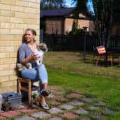 Terhi Vallineva istuu asuntonsa takapihalla puutarhatuolissa. Aurinko paistaa ja Vallineva pitää sylissään Börje-koiraa.
