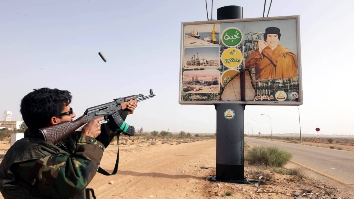 Libyan kapinallissotilas ampuu kohti Mammar Gaddafin mainosta.