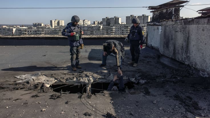 Suojavarusteisiin pukeutuneet henkilöt auttavat asukasta ulos talon katossa olevasta reiästä.