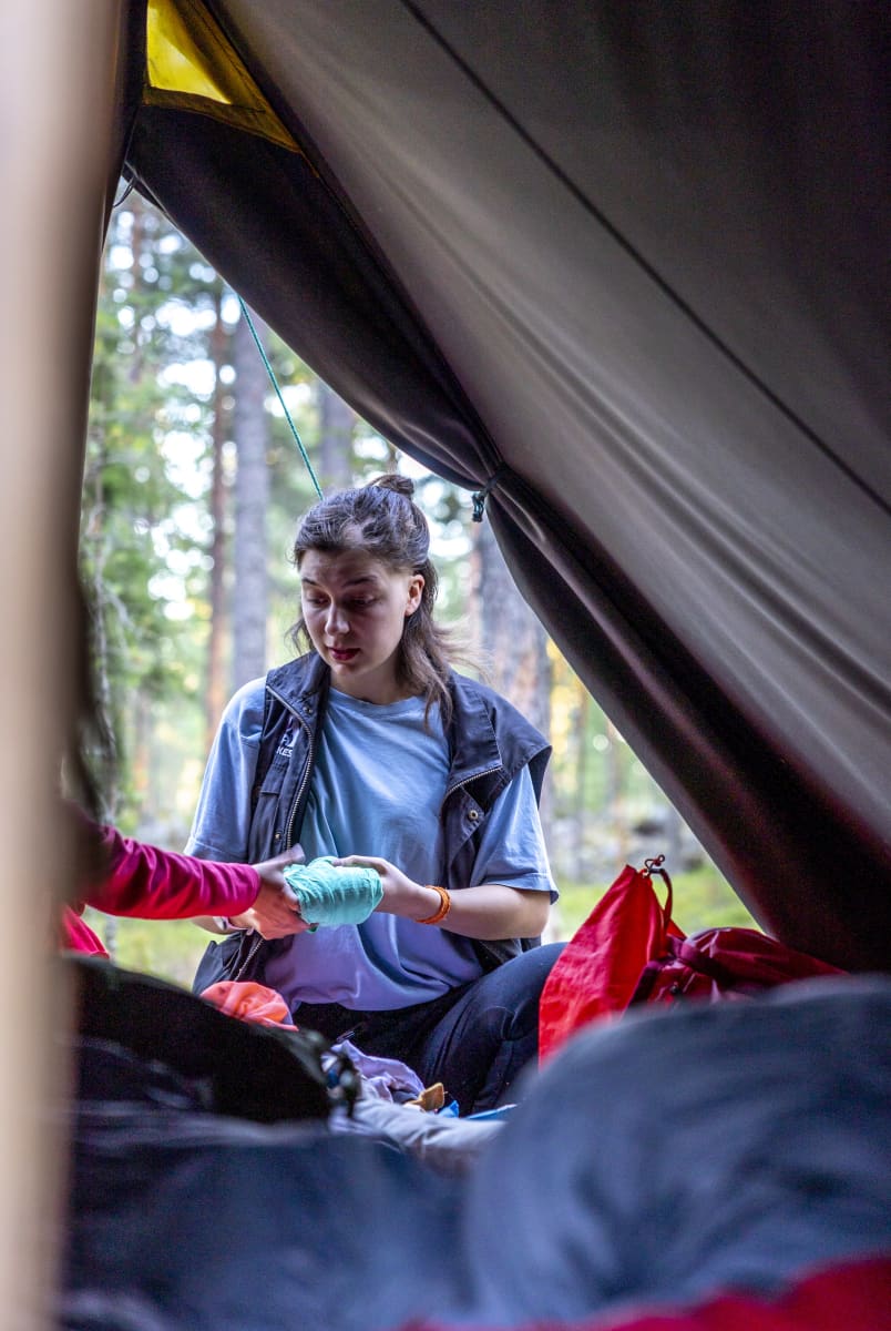 Leiriohjaaja auttaa lasta etsimään vaatteitaan teltan suuaukolla.