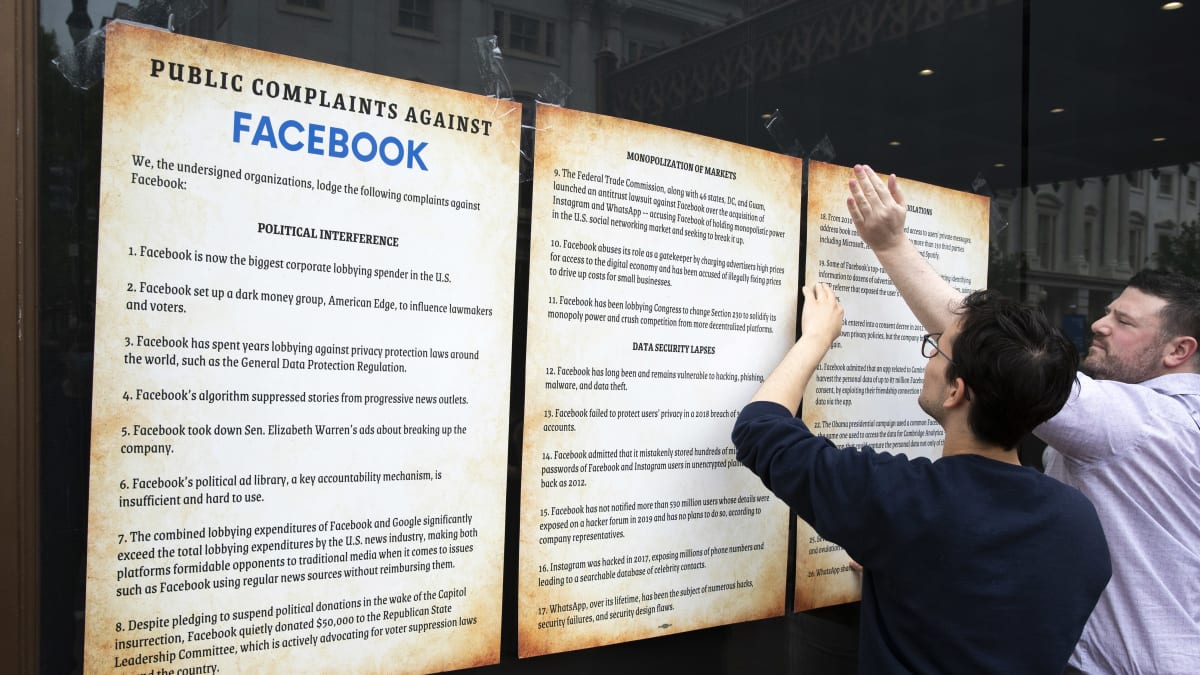 Aktivistit laittavat ikkunaan kiinni julisteita joissa kerrotaan valituksista Facebookkia vastaan.