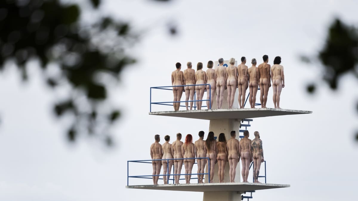 A group of naked people standing on a diving platform.