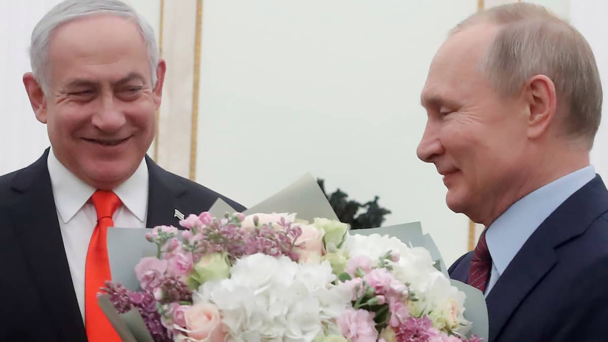Israelin pääministeri Benjamin Netanjahu ja Venäjän presidentti Vladimir Putin hymyilevät vierekkäin. Putinilla on kädessään kukkakimppu.