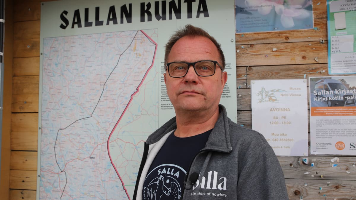 Sallan kunnanjohtaja Erkki Parkkinen seisoo ilmoitustaulun edessä ulkona. Ilmoitustaululla on Sallan kartta.