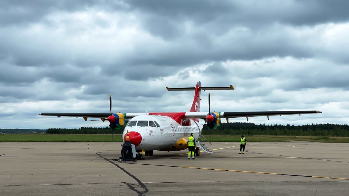 Danish air transport -yhtiön (DAT) punavalkoinen ATR-potkuriturbiinikone Kajaanin lentokenttätasolla, taustalla taivaalla synkkiä sadepilviä.