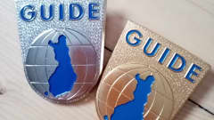 Oppaan hopeoitu merkki, jossa kuvattuna Suomi karttapiirroksena ja ylhäällä sana Guide. 