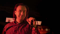 Jussi Majaniemi seisoo mikrofoni kädessään punaisella valolla valoistulla Popparin lavalla Jyväskylässä. 