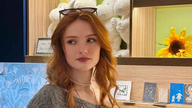 Nuori nainen seisoo seinähyllyn edessä, jossa on muumeja.