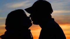 Man och kvinna kysser varandra framför solnedgång