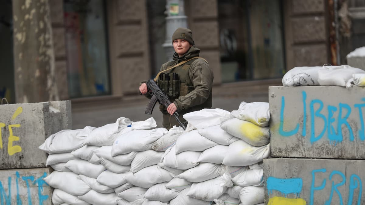 Ukrainalainen naissotilas seisoo vartiossa hiekkasäkkien takana. 