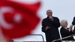 Recep Tayyip Erdoğan puhuu kannattajilleen korokkeella, etualalla punainen Turkin lippu.