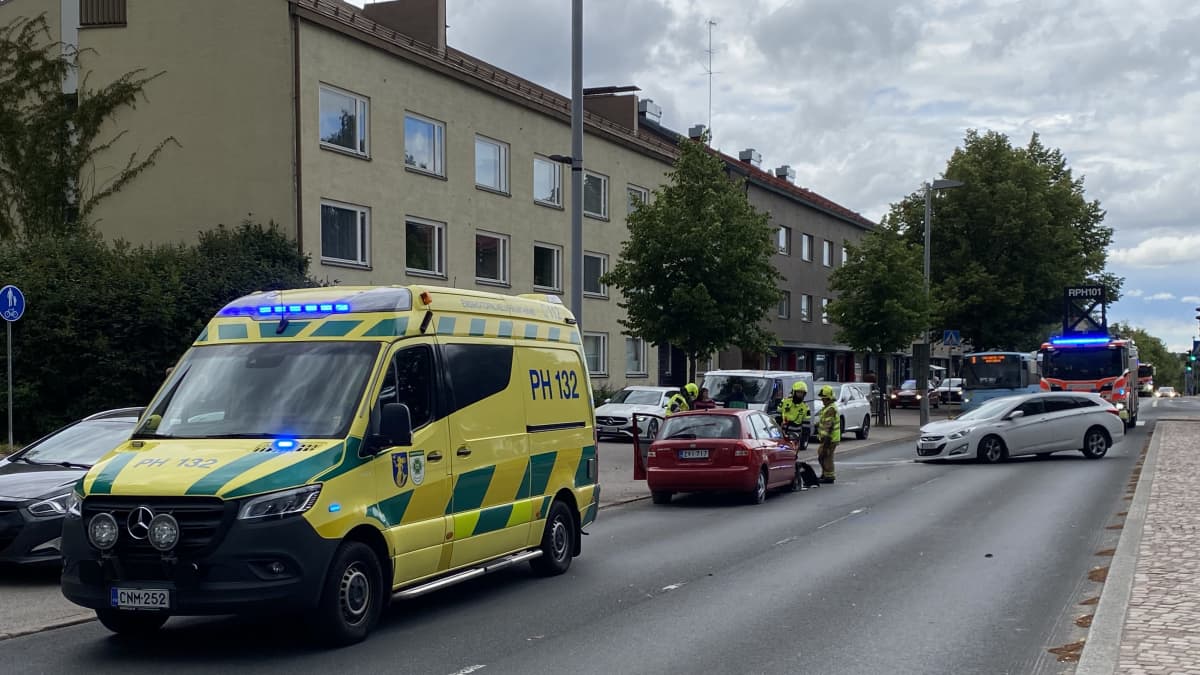 Kuvassa ambulanssi vilkut päällä, kaksi kolaroitua autoa ja paloauto taka-alalla.