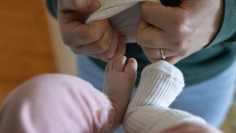 A woman putting a sock on a baby's foot.
