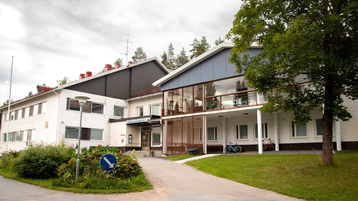 Ruoveden terveyskeskus kuvattuna pääovien edestä. Keskellä pihaa kukkaistutuksia, rakennuksessa muun muassa iso lasitettu parveke.
