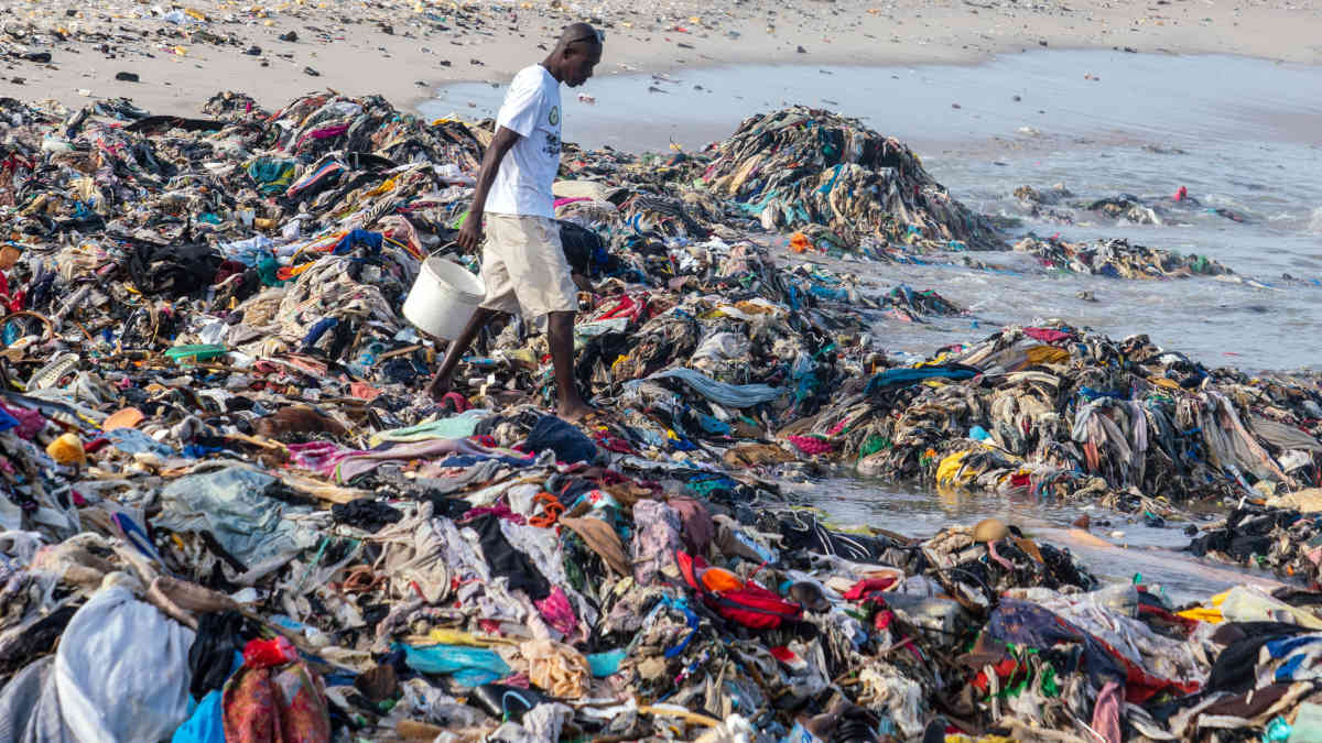 Mies kävelee rannalle huuhtoutuneiden kierrätysvaatteiden keskellä lähellä Ghanan pääkaupunkia Accraa.