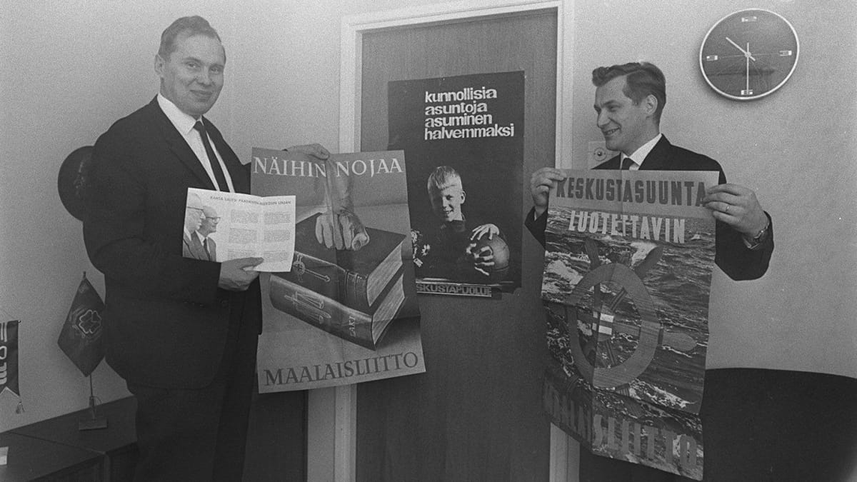 Kaksi mustaan pukuun pukautunutta miestä esittelevät Maalaisliiton vaalimainoksia.