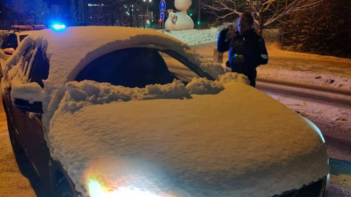 Luminen auto ja poliisi katsoo taskulampulla auton sisälle.