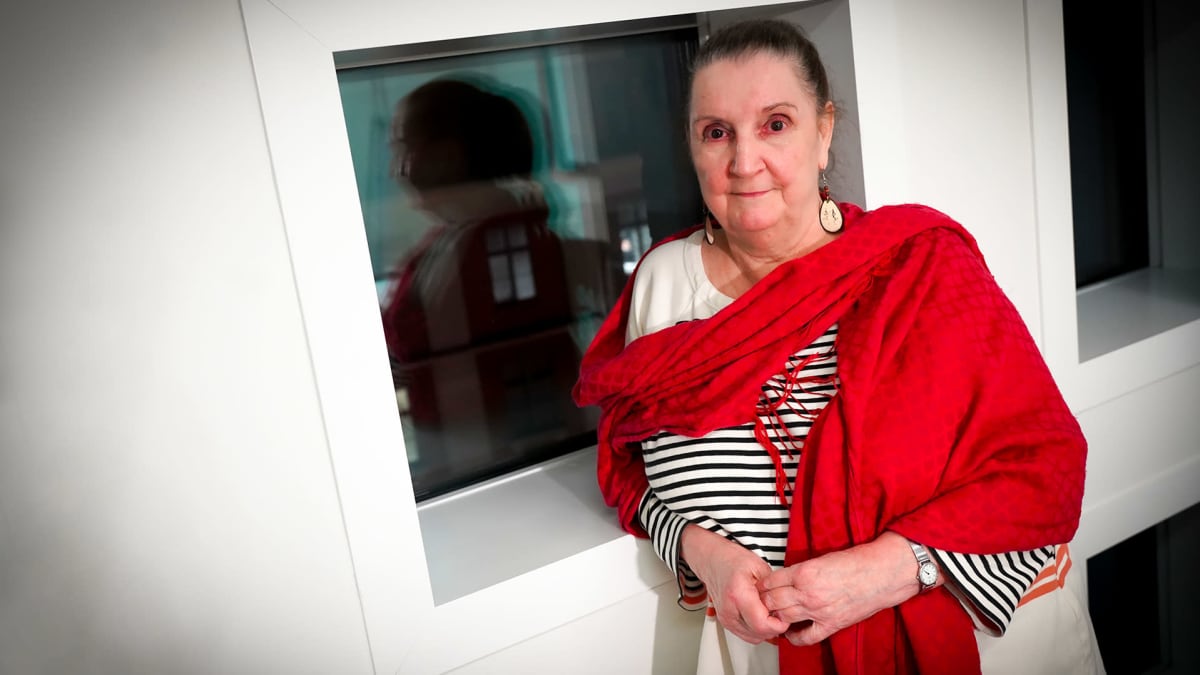Väitöskirjatutkija Elisa Mikkola valkoisessa huoneessa mustan ikkunan ääressä. 