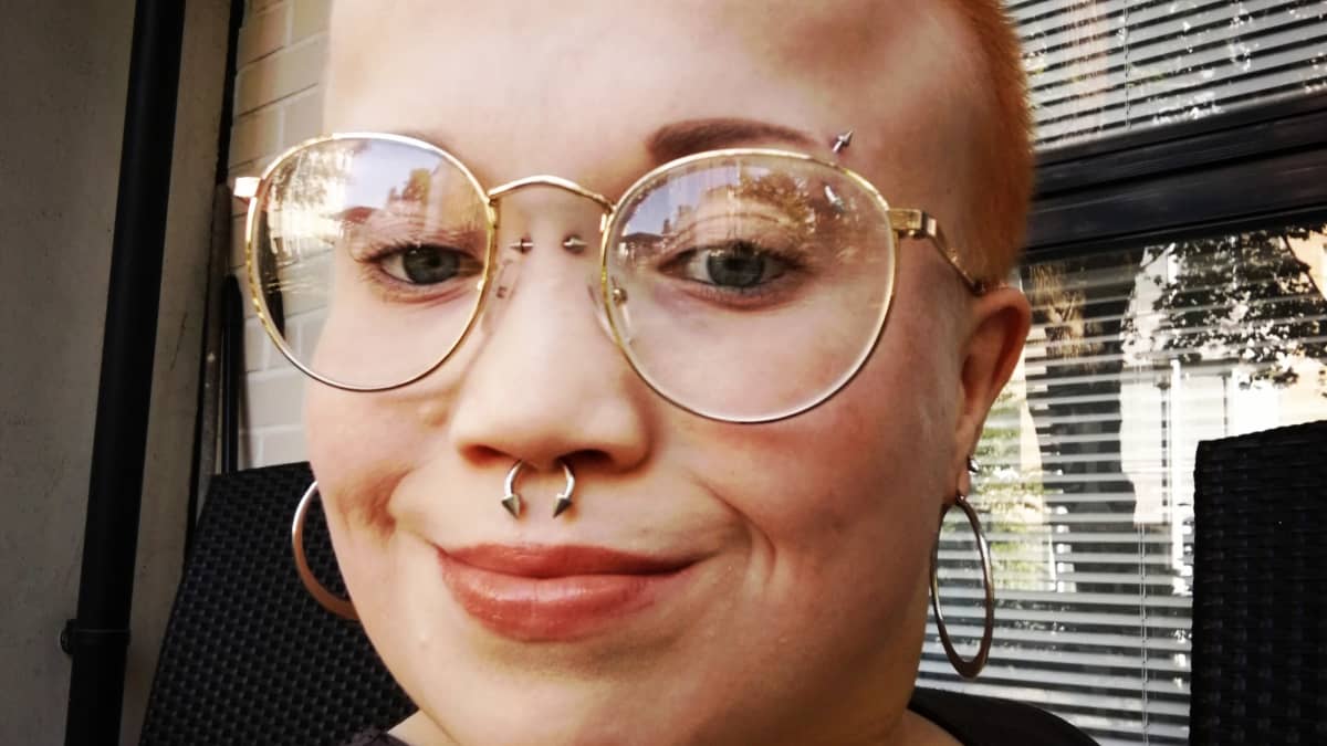 Selfie Elina Kurvista, jolla on silmälasit, lyhyt punertava tukka ja lävistyksiä.