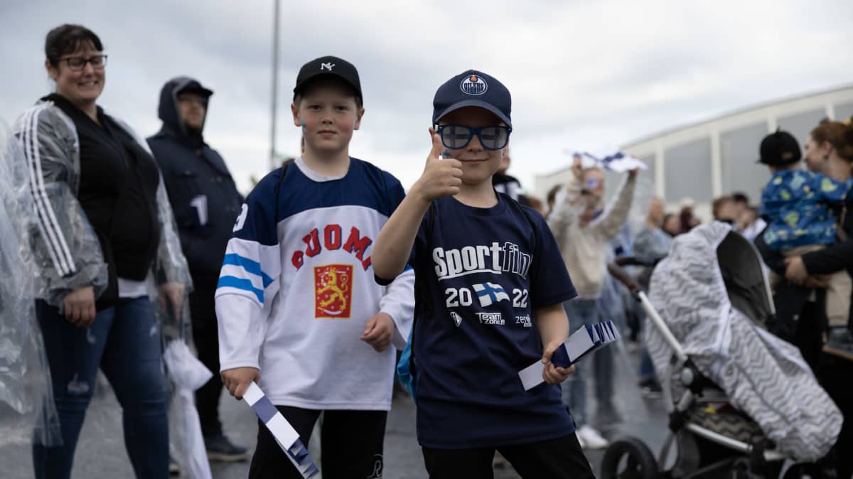 Kaksi poikaa fanituotteet yllään näyttää peukkua kameralle. Taustalla kiekkojuhlakansaa.