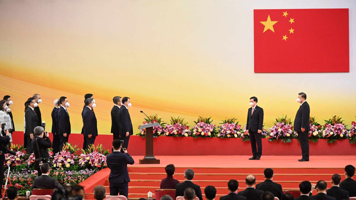 Pukuihmisiä seisoo lavalla rivissä. Kaksi kauempana toisista. Taustalla kiinan lippu.
