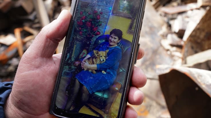 Miehen kädessä puhelin jossa kuva naisesta koira sylissä