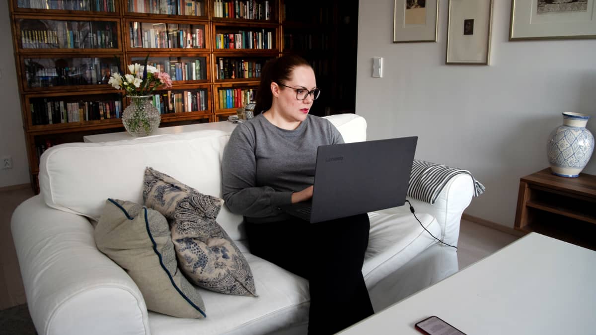 Pauliina Eriksson katsoo kannettavaa tietokonetta kotisohvallansa.