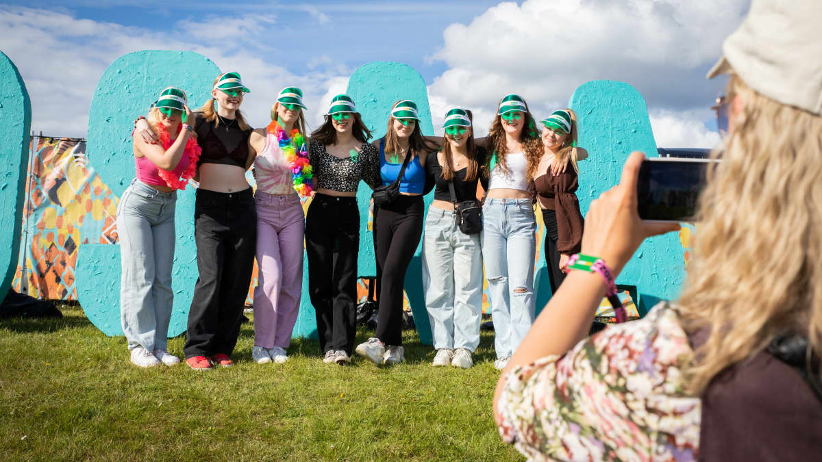 Joukko nuoria naisia otattaa itsestään valokuvaa suuren Ilosaarirock-tekstin edessä.