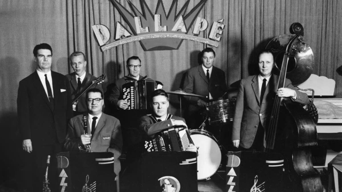 Dallapé-orkesteri ryhmäkuvassa. Taustakankaassa yhtyeen nimilogo.