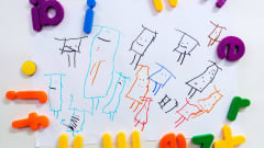 Päiväkodin ilmoitustaululla lasten piirros kiinnitettynä kirjainmagneeteilla.