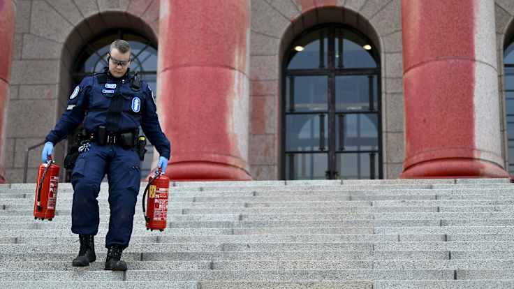 Eduskuntatalon pylväät on maalattu roiskien punaisella maalilla. Poliisi kantaa kahta punaista vaahtosammutinta alas portaita.