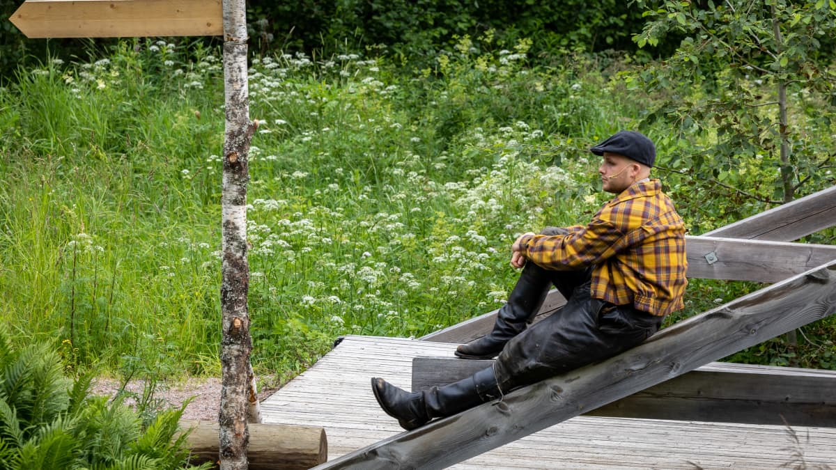 Ihmiset suviyössä -esityksen Nokia -nimistä hahmoa esittävä Tuomas Miettola roolissaan istumassa sillalla lavasteissa.