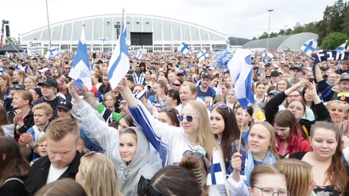 Hakametsän hallin edustalla parkkialue täynnä ihmisiä, joista iso osa heiluttaa Suomen lippuja.